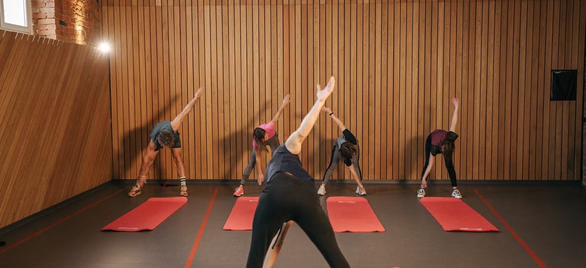 Yoga class with diverse adults stretching on mats in a cozy wooden studio.